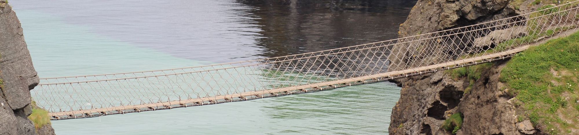 A rope bridge spanning a sea chasm between two rocky cliffs